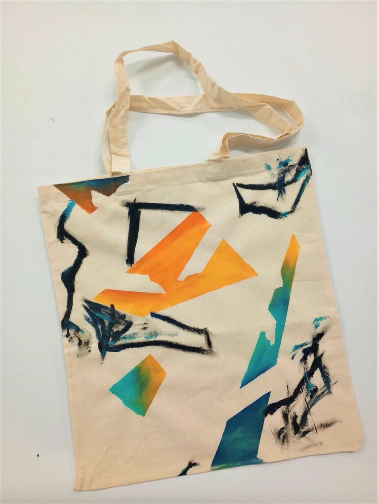 Photograph of a canvas tote bag with multicolored stamps and designs painted on. 